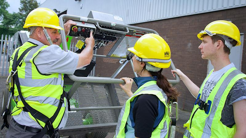 An IPAF mobile elevating work platform (MEWP) instructor showing trainees the controls in the basket.